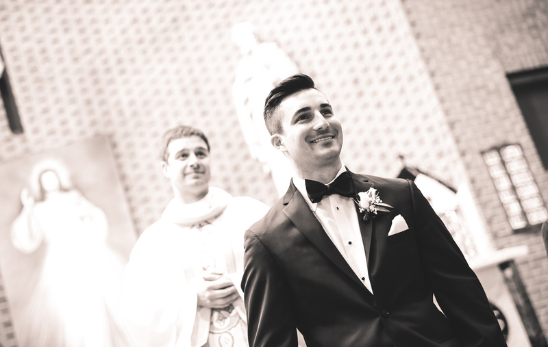 Wedding photography, a beaming groom awaits his bride. The priest stands behind him. 