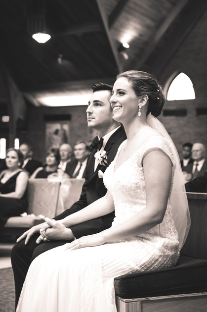 Wedding photography, a bride and groom sit in a church holding hands and smiling. 