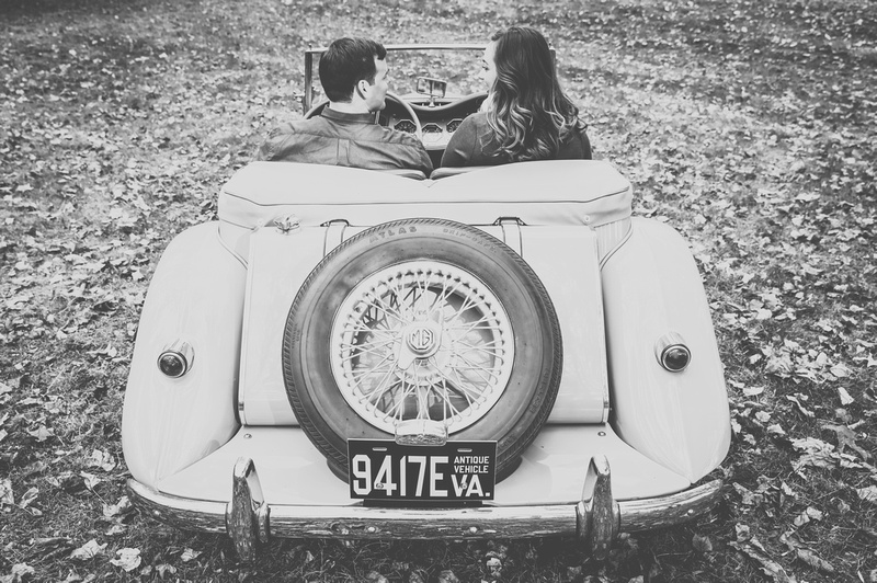 Engagement photography: a young couple sits behind the wheel of an antique car, we see it from behind. 