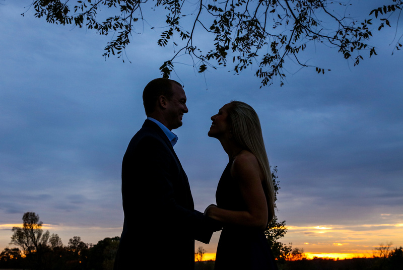 The silhouette of a young couple at sunset. They are holding hands and smiling at each other. 