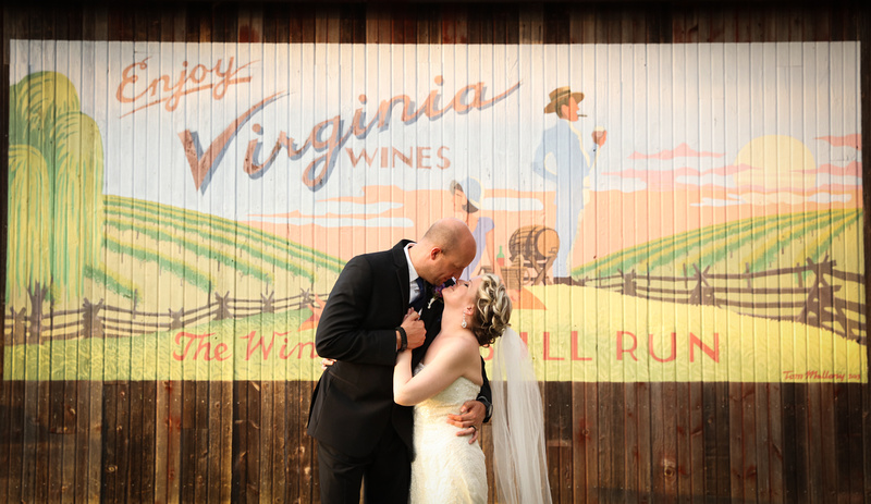 Wedding photography, a groom gazes at his bride while holding her hand. They stand in front of a barn in Virginia. 