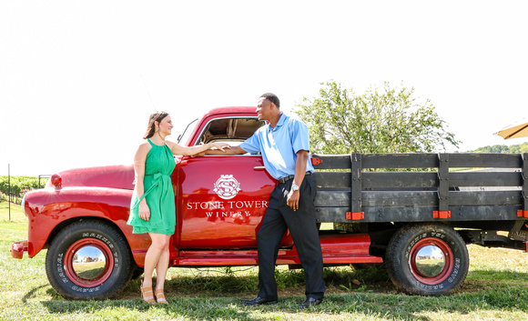 Engagement photography: a woman in a green dress and a man in a blue shirt stand beside a red farm truck. 