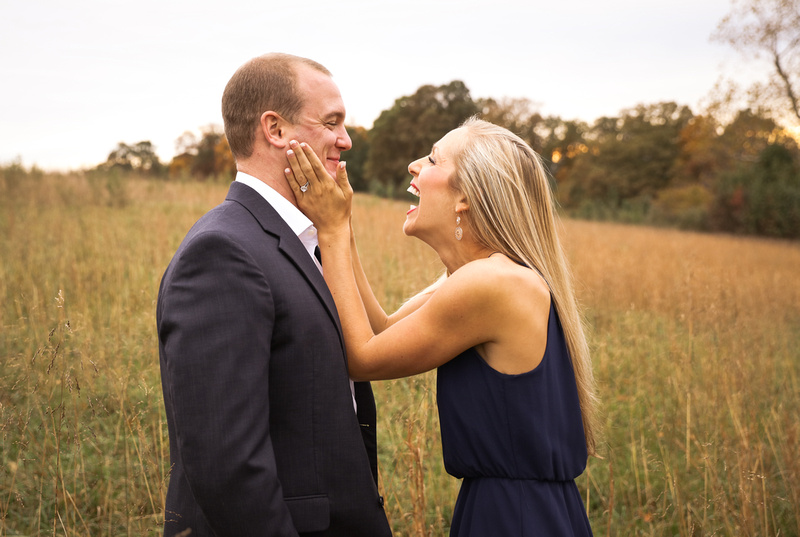 Engagement photography, a young woman in a navy dress holds her fiance's face and laughs. 