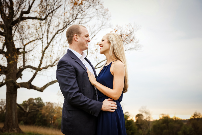 Engagement photography, a young lady in a blue dress and man in a navy blazer embrace. 