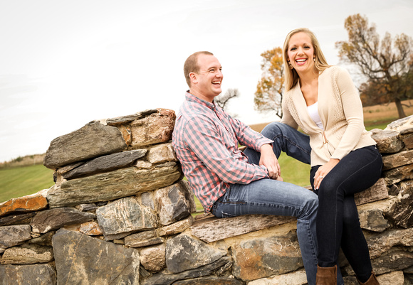 Engagement photography, a couple laughs out loud while sitting on a stone wall. 