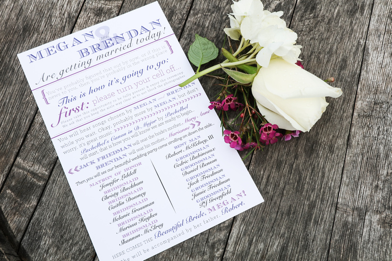 Wedding photography, a wedding invitation sits on a wooden barrel next to white and purple flowers. 
