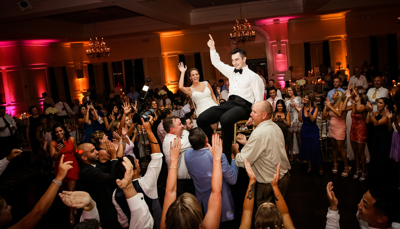 Wedding photography, a bride and groom are lifted up on chairs on a large dance floor. 