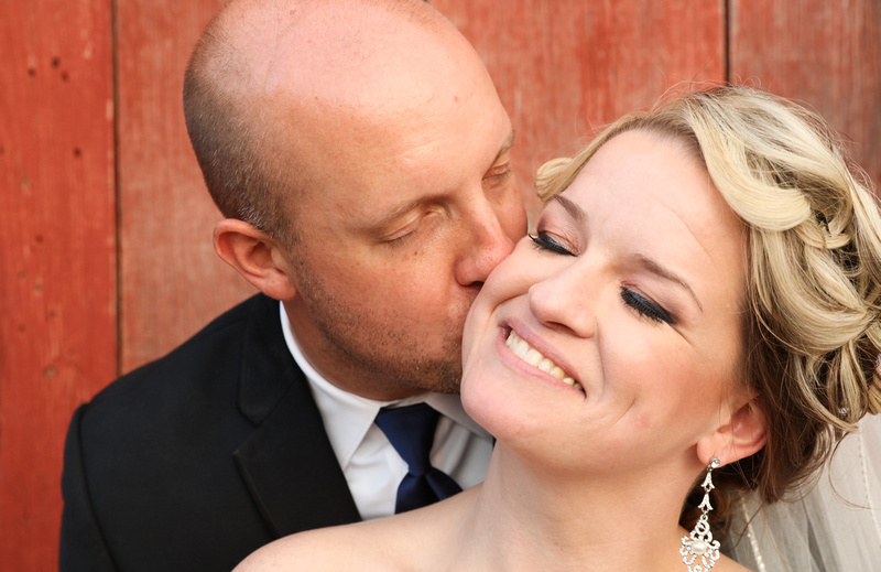 Wedding photography, the bride smiles serenely as her husband kisses her cheek. 