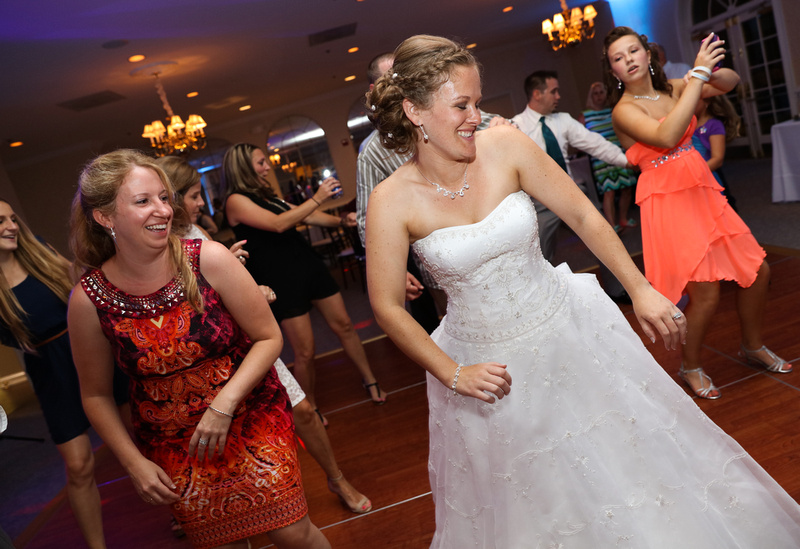 Wedding photography, a bride laughs while on the dance floor. Women are dancing behind her in orange and black dresses. 