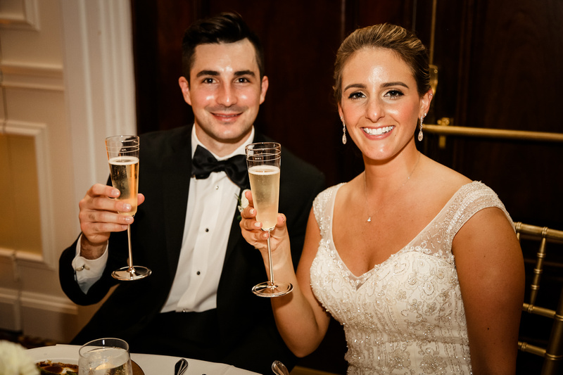 Wedding photography, the bride and groom smile at the camera while holding champagne flutes. 
