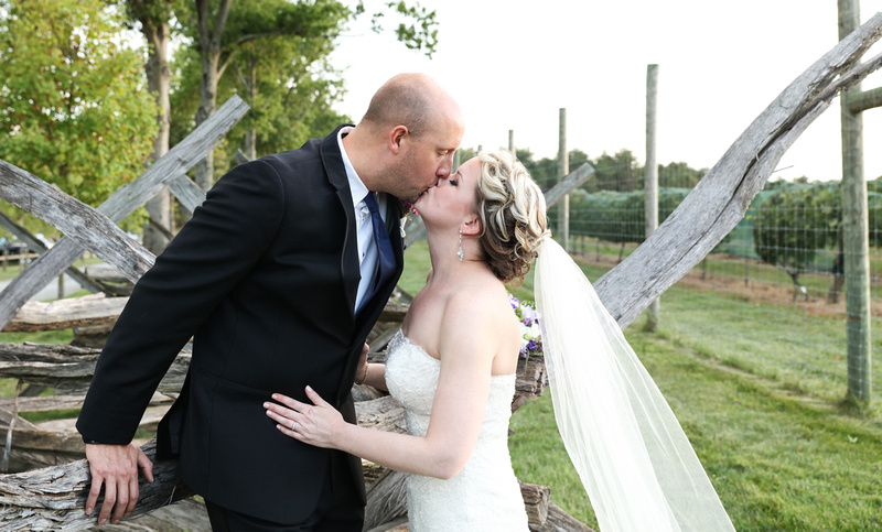 Wedding photography, a bride and groom kiss while leaning on a historic wooden fence. 