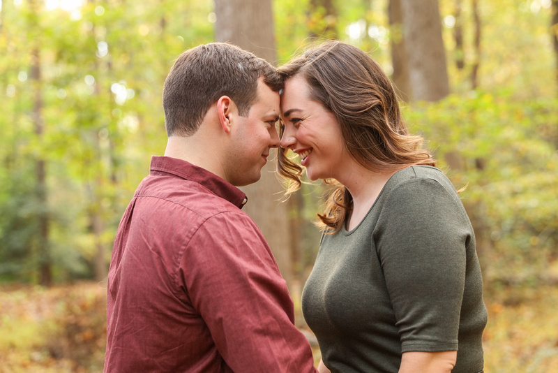 Engagement photography: a young couple in the woods laughs and puts their foreheads together.