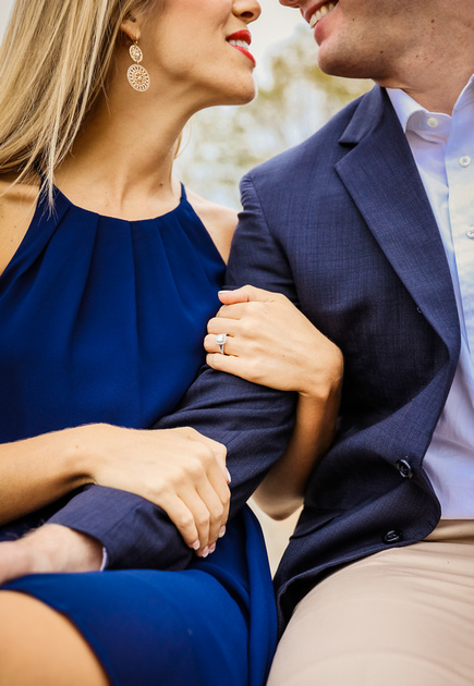 Engagement photography, a closeup of a couple's arms intertwined. She wears a diamond ring. They are smiling at each other.  