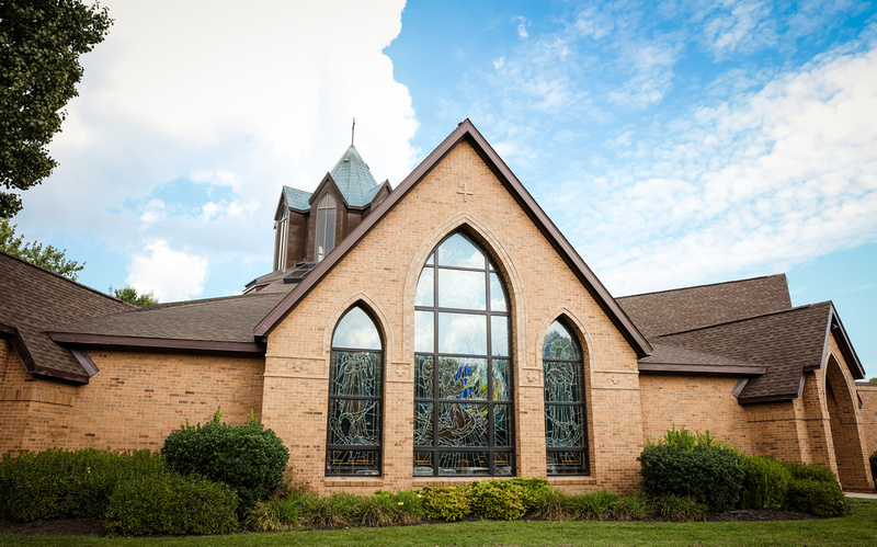 Wedding photography, a Catholic church with large stained glass windows. The sky is blue with white clouds. 