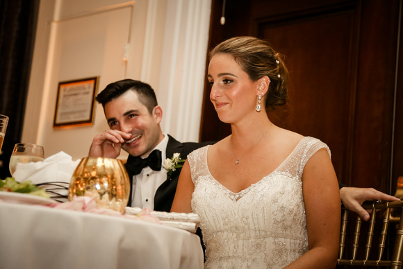 Wedding photography, the bride and groom laugh at their table while listening to speeches. 